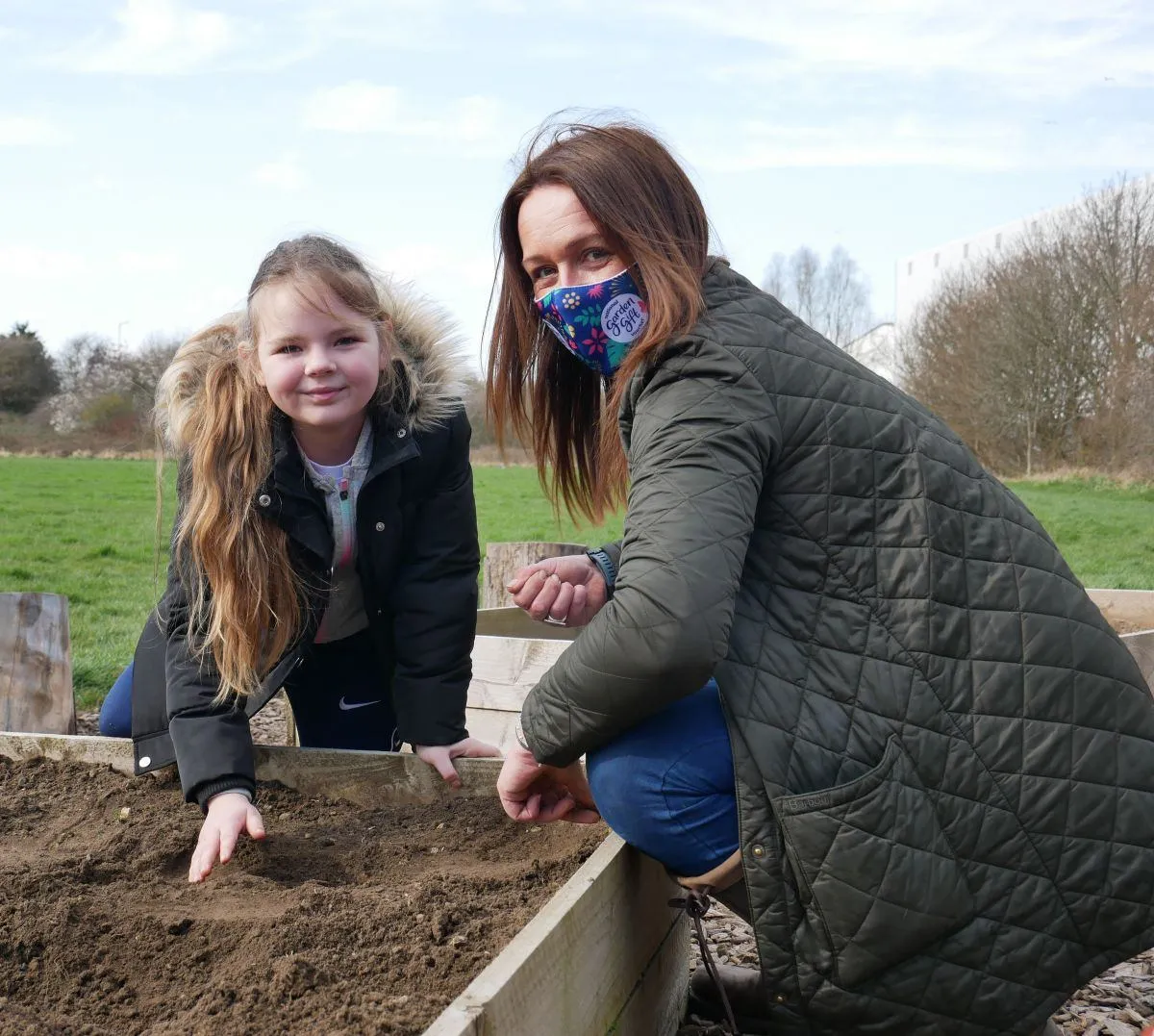Young woman and child planting seeds in a raised flower bed