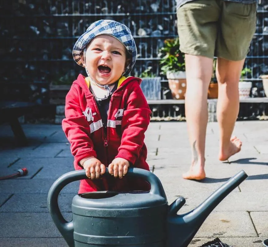 Toddler laughing and holding a watering can