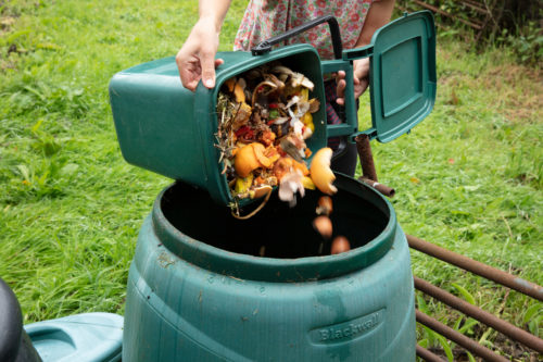 A woman emptying a home composting bin into an outdoor compost bin to reduce waste