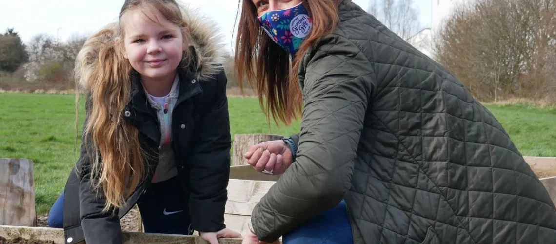 Young woman and child planting seeds in a raised flower bed